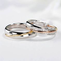 two gold and silver wedding rings with diamonds on the inside of each ring, sitting on a white surface