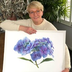 a woman holding up a painting with blue flowers on it