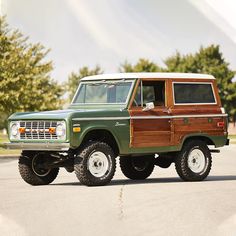 a green and brown truck parked on top of a parking lot next to some trees