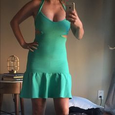 a woman in a green dress taking a selfie with her cell phone while standing next to a bed