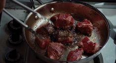 meat is being cooked in a frying pan on the stove top with tongs