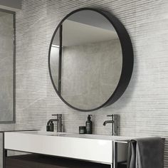 a bathroom sink under a round mirror in front of a white brick wall with black accents