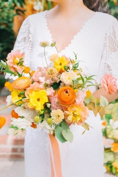 a woman holding a bouquet of flowers in her hands and wearing a white dress with an orange sash around her waist