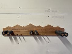 a wooden shelf with three black handles and four metal knobs on it, hanging from the wall