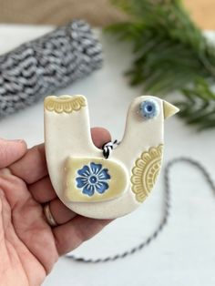 a hand holding a ceramic bird ornament with blue flowers on it's tail