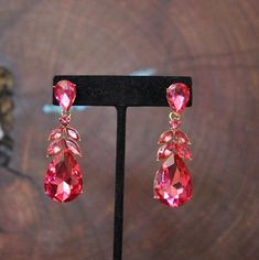 a pair of pink earrings sitting on top of a black stand next to a tree