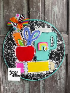 a paper plate with scissors, an apple and other items on it hanging from a wooden wall