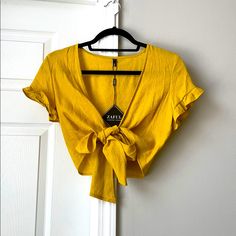 Yellow Tied Cropped Blouse, So Many Different Ways To Tie And Wear This Shirt The Options Are Endless! Loose, Tight, High, Low, Bow In Front, Knot In Back, Really Anyway! Size Medium But Fits Any Size S-L Because It Is Adjustable New With Tags, Never Worn, Great Yellow (Almost Mustard But Not So Dark) Color Tied V-neck Tops For Vacation, Chic Yellow V-neck Crop Top, Summer V-neck Tied Tops, Trendy Summer Tops With Tie Waist, Casual Beach Tops With Tied Details, Summer V-neck Top With Tie Waist, Trendy Tie Waist Top For Summer, Casual Tied Tops For Beach, Chic Summer Tied Blouse