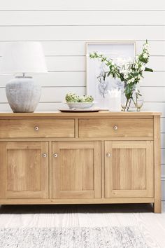 a wooden cabinet with two vases on top of it next to a lamp and pictures