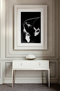 a white table with a bowl on it in front of a framed black and white photograph