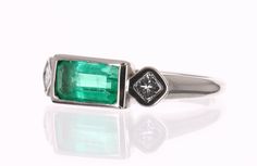 A Colombian emerald and princess cut three stone ring. Dexterously handcrafted in gleaming 18K white gold, this ring features a 1.40-carat natural elongated emerald, emerald cut from the famous Muzo mines. Set in a secure bezel setting for extra protection. This extraordinary emerald has stunning bluish-green color and an incandescent glow. The emerald has beautiful clarity with natural Jardins that occur in all earth mined emeralds. Bezel set, princess cut diamonds accent the center gem. This r Three Stone Rectangular Diamond Jewelry, Rectangular Three Stone Diamond Jewelry, Fine Jewelry With Three Stone Rectangular Design, Fine Jewelry Rectangular Three Stone, Fine Jewelry Rectangular Three-stone, Elegant Rectangular Three-stone Jewelry, White Gold Three Stone Rectangular Jewelry, Rectangular Three Stone White Gold Jewelry, Multi-stone Platinum Jewelry With Emerald Cut