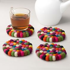 four coasters with different colored circles next to a cup of tea and white pitcher