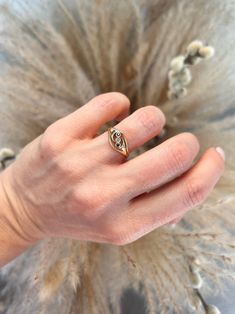 a woman's hand with a gold ring on top of her finger and feathers in the background