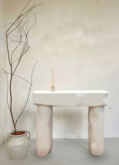 a white table with a candle on it next to a potted plant and vase