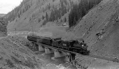 black and white photograph of a train going over a bridge on the side of a mountain