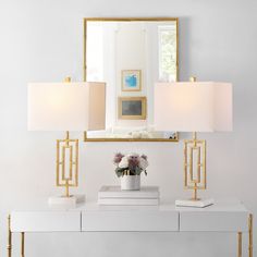 a white console table topped with two lamps and a mirror over it, next to a vase filled with flowers