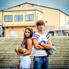 a man and woman standing next to each other in front of bleachers holding footballs