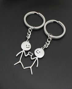 two metal key chains that are shaped like people with faces and hands, one holding the other