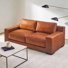 a brown leather couch sitting in a living room next to a coffee table and lamp