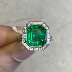 an emerald and diamond ring is being held