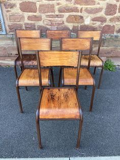 six wooden chairs sitting next to each other on the ground in front of a brick wall