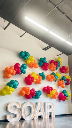 the word soar is surrounded by balloons and streamers in front of a white wall