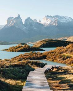 a wooden walkway leading to a lake with mountains in the background