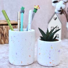 two white cups with pens and pencils in them