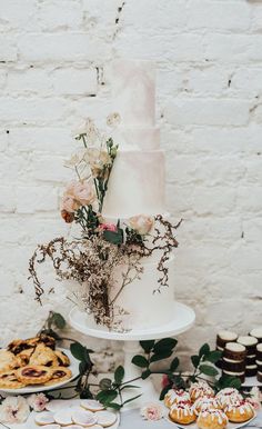 a wedding cake and desserts on a table with white brick wall in the background