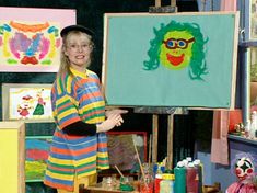 a woman standing in front of an easel with paintings on it