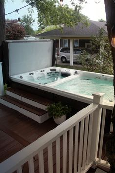 a hot tub sitting on top of a wooden deck next to a white fence and tree