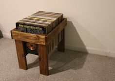 a small wooden table topped with lots of records next to a white wall and floor