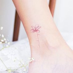 a woman's foot with a small pink flower tattoo on her left side ankle