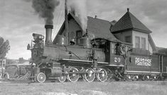 black and white photograph of an old steam engine on the tracks in front of a house