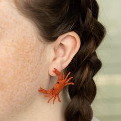 a close up of a person wearing earrings with an orange crab on it's ear