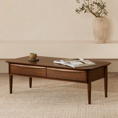 a coffee table with a book and vase on top in front of a beige wall