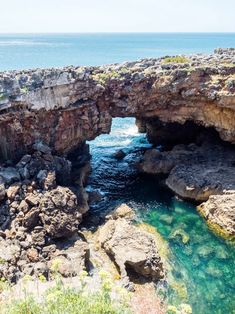 the water is crystal clear and blue in this rocky area with an arch over looking the ocean