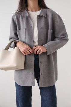 a woman holding a white purse and wearing a gray coat