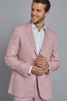 a man in a pink suit and white shirt is smiling at the camera while standing against a gray background