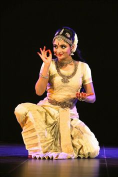 a woman sitting on top of a wooden floor holding her hand up in the air