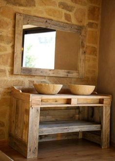 a wooden table with two bowls on it and a mirror hanging above the table, in front of a stone wall