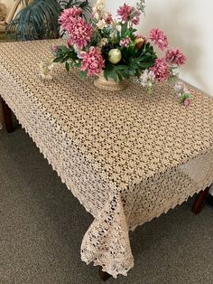 there is a table with a crocheted cloth on it and flowers in a vase