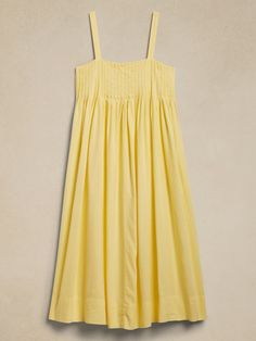 a yellow dress hanging on a hanger in front of a beige wall with a white background