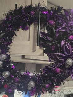 a wreath with purple and silver decorations hanging from the front of a kitchen cabinet door