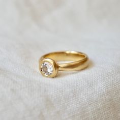 a yellow gold ring with a single diamond on the top, sitting on a white cloth