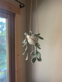 a crocheted plant hanging from a hook on a wall next to a window