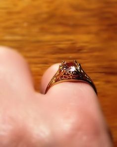 a person's hand holding a ring with a stone in it on top of a wooden table