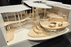 a model of a house made out of wood and white plastic with people standing around it