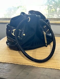 This Cole Haan Equestrian Drawstring shoulder bag is a stylish and versatile addition to any wardrobe. The bag features a pebbled black leather exterior with brass hardware, braided handles, and a drawstring closure. It has a large size of 15 inches in width, 10 inches in height, and 9 inches in depth, making it suitable for various occasions such as travel, parties, casual outings, and business meetings. The bag also has several features, including a lined interior with inner pockets and a key Drawstring Shoulder Bag, Black Pebbles, Classic Bags, Cole Haan, Large Bags, Pebbled Leather, Purses And Handbags, Equestrian, Bags Designer