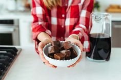 a woman holding a bowl full of chocolates next to a cup of coffee on a counter